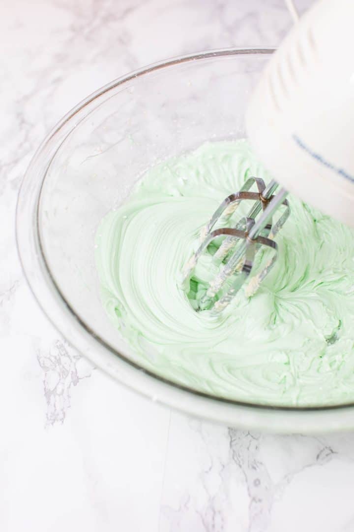 Green frosting in large bowl being whipped up with hand beaters