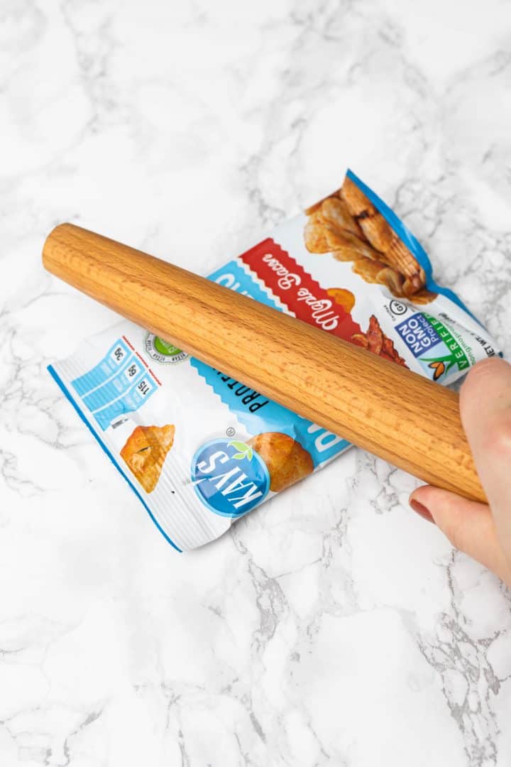 Hand smashing bag of chips with rolling pin
