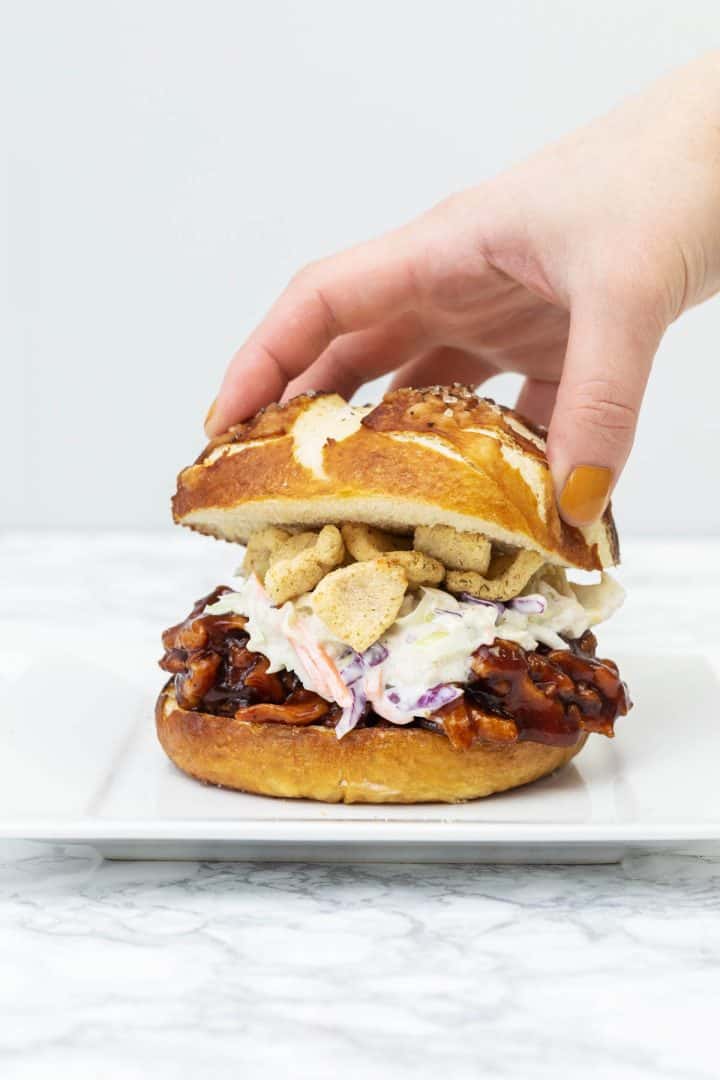 Hand placing top of pretzel bun on barbecue sandwich