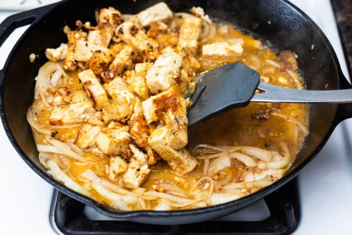 Cooked tofu with onions in sauce in cast iron pan on stovetop