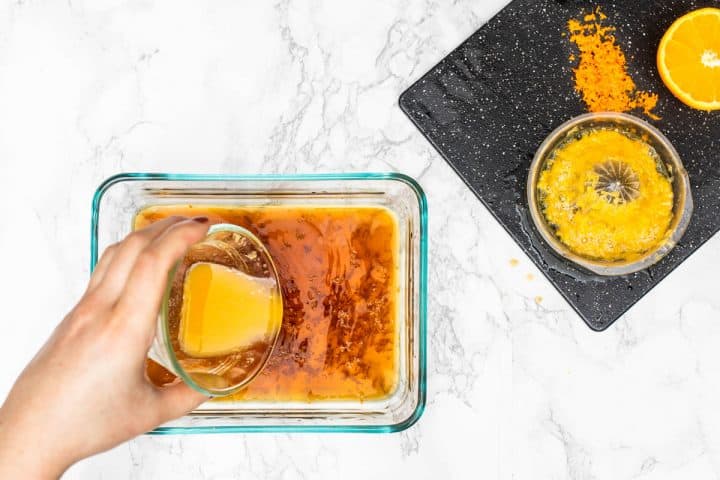 Hand pouring orange juice in marinade with orange zest and pulp on cutting board off to side