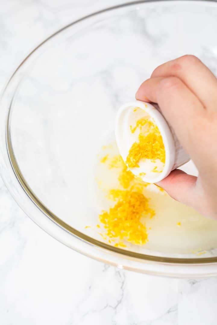 Hand pouring lemon zest into mixing bowl