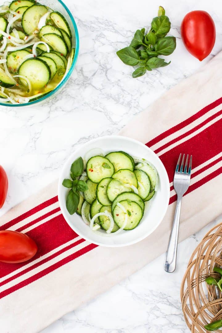 Bowl of cucumber and onion salad on towel with tomatoes
