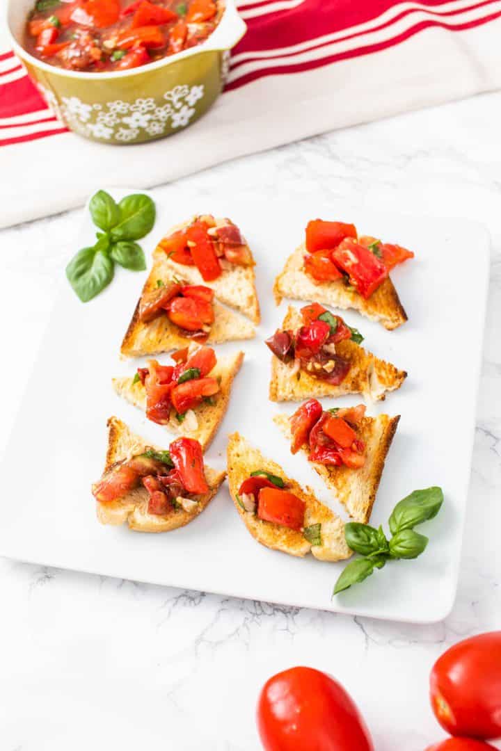 Tomato bruschetta on pieces of toast on plate with basil and tomatoes