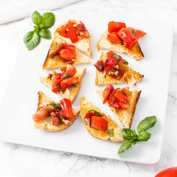 Tomato bruschetta on pieces of toast on plate with basil and tomatoes