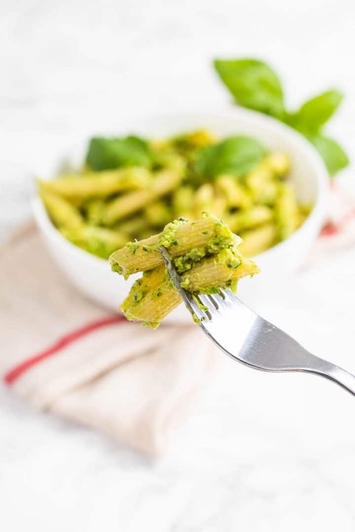 Close up of pesto pasta on fork with bowl in background