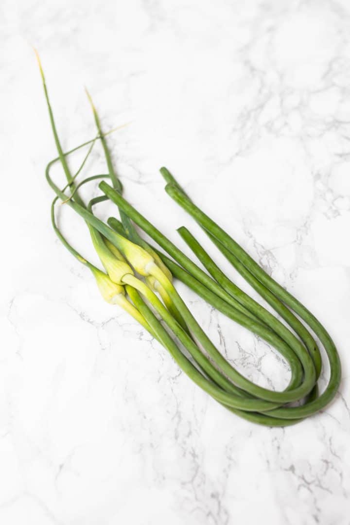Bundle of garlic scapes on white marble surface