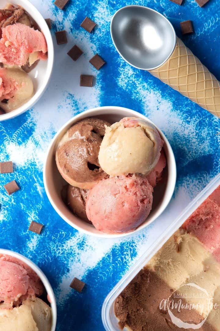 Bowl of Neapolitan ice cream on blue tablecloth with ice cream scoop