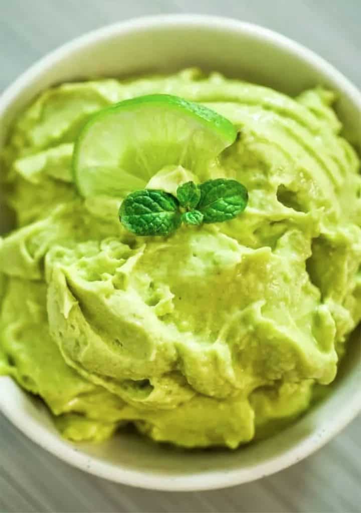 Bowl of avocado ice cream garnished with mint leaf and lime slice