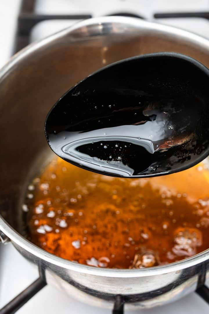 Brown sugar syrup bubbling on stove with spoon showing syrup consistency