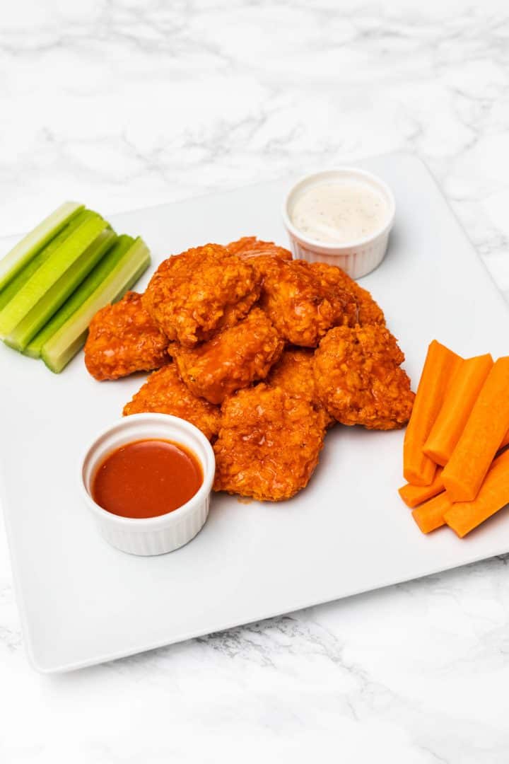 Plate of buffalo tofu wings on plate with celery sticks, carrot sticks, ranch dressing, and buffalo sauce