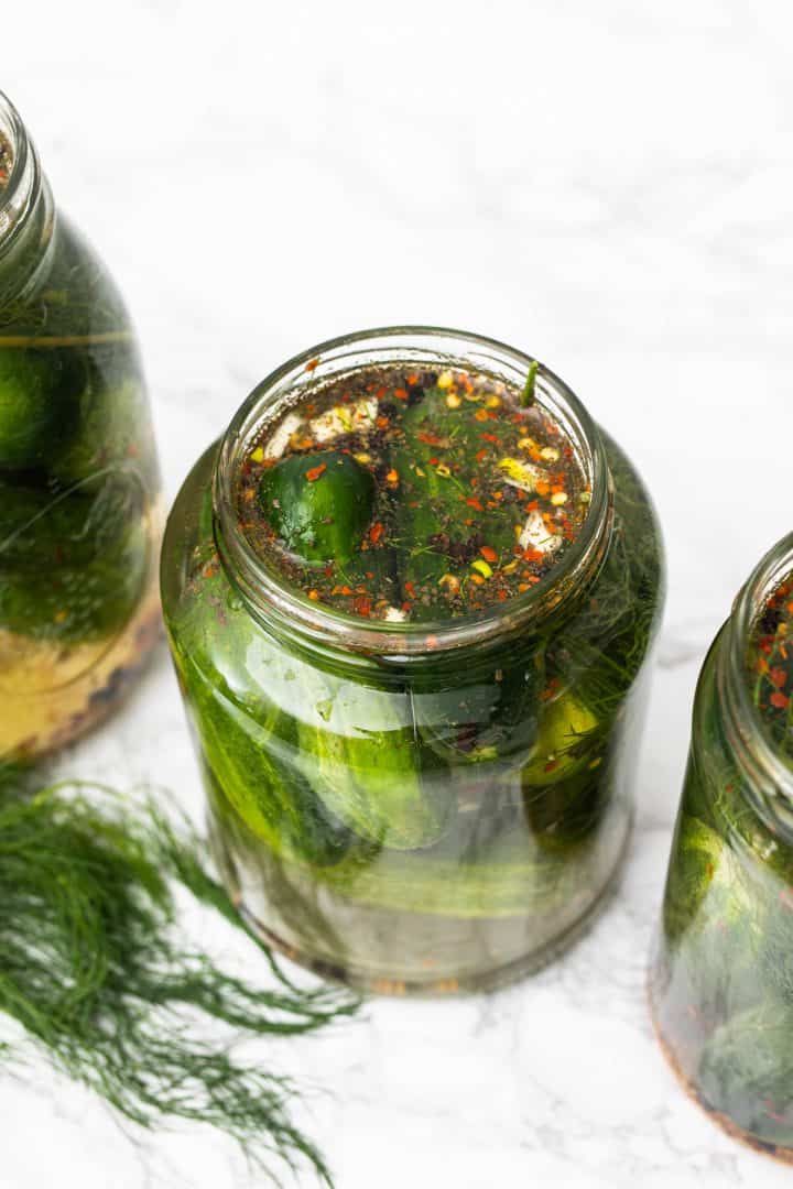 Three jars of homemade dill pickles with chili flakes