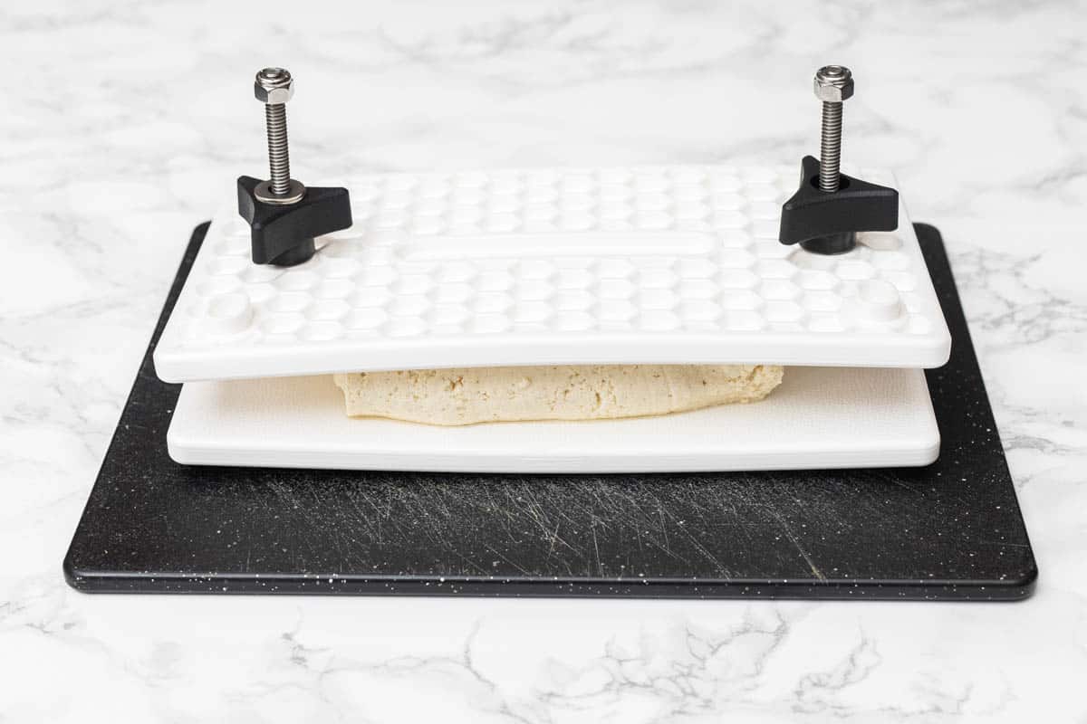 Pressed tofu in tofu press on cutting board on white marble counter