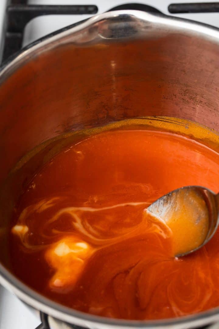 Spoon stirring margarine into buffalo sauce in saucepan over the stove