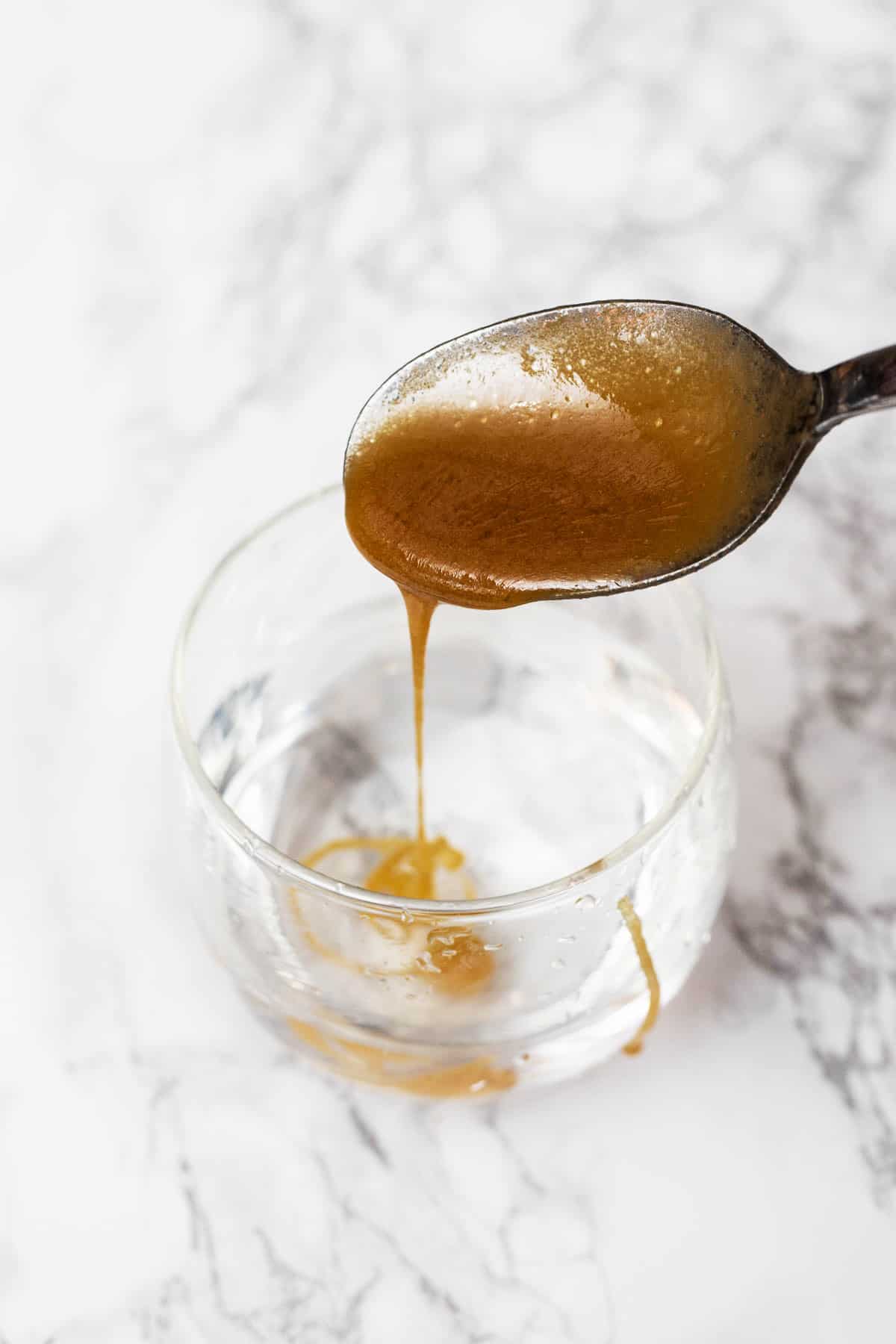 Caramel dripping off metal spoon into glass of water
