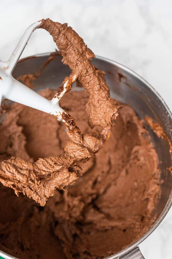 Prepared chocolate frosting in bowl and on paddle attachment of stand mixer