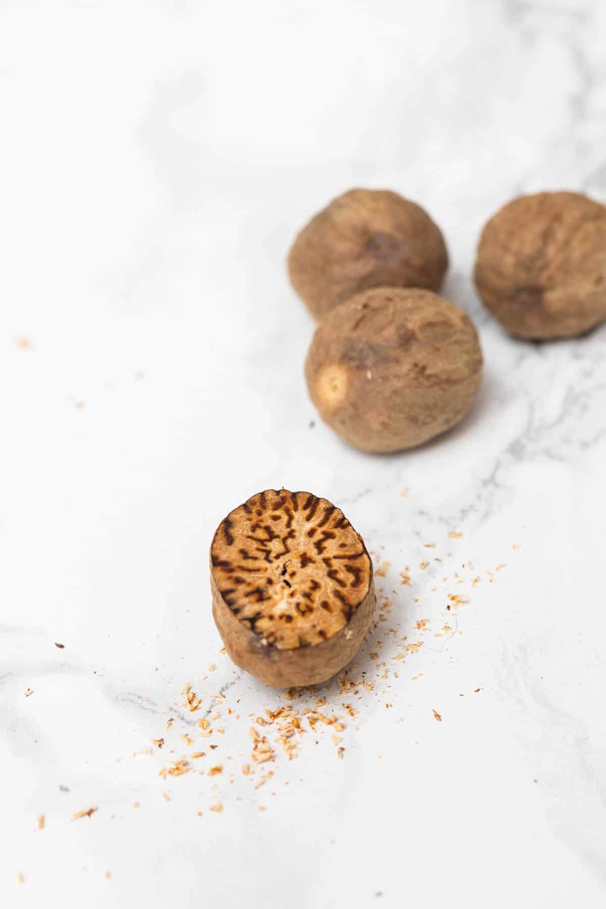 Grated fresh nutmeg showing inside with pile of nutmeg in background