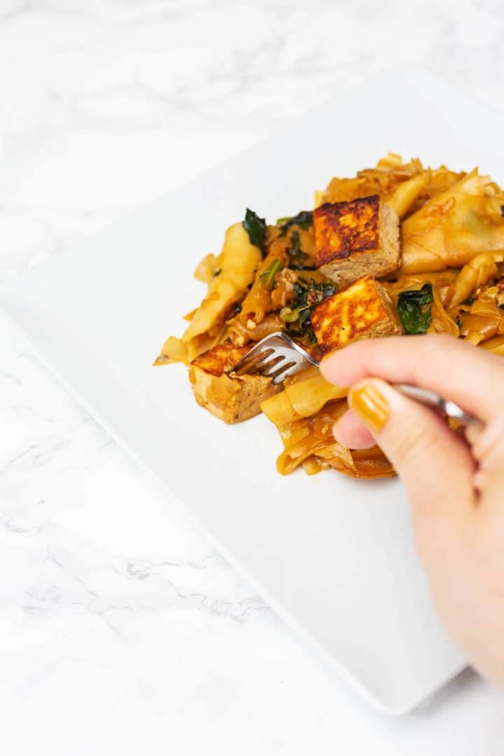 Hand sticking fork into plate of tofu Pad See Ew