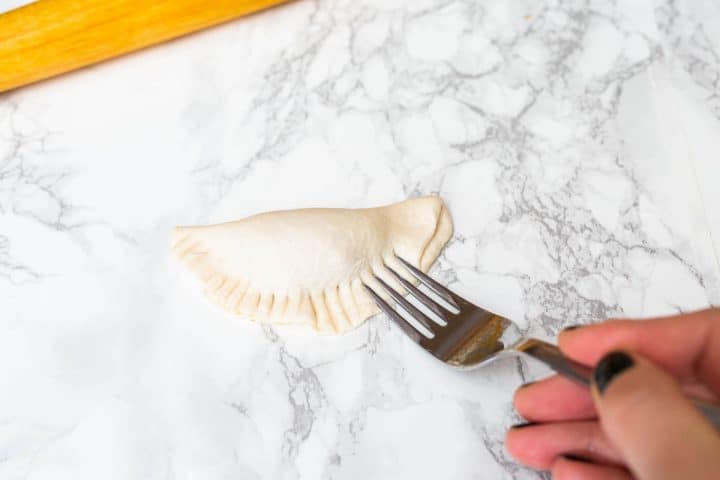 Hand sealing pierogi with fork on counter