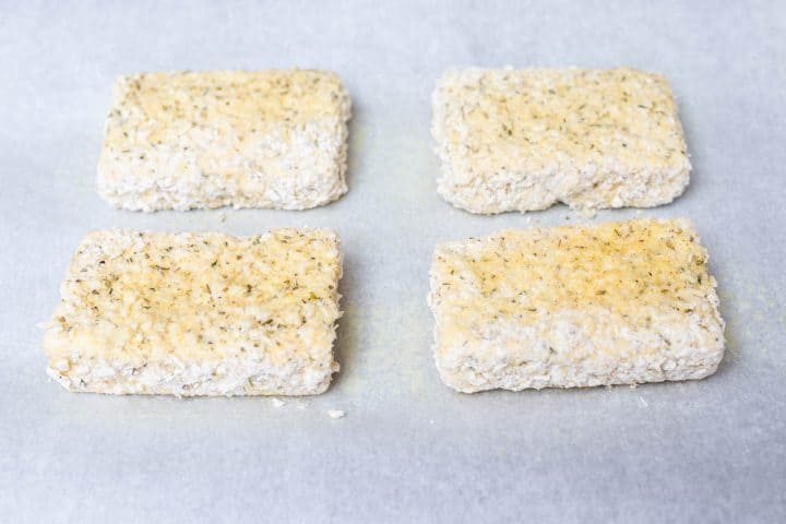 Uncooked breaded tofu on parchment paper on baking sheet