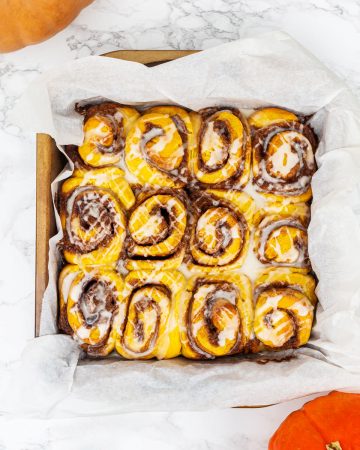 Overhead image of tray of vegan pumpkin cinnamon rolls with glaze and pumpkins off to side