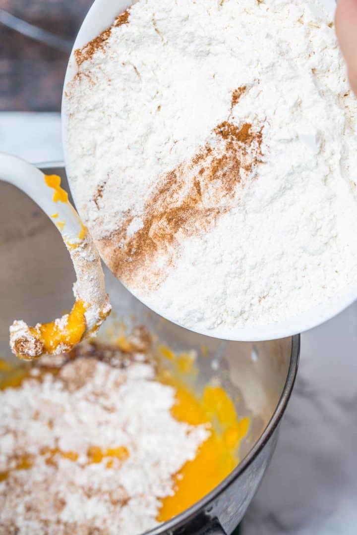 Pouring bowl of flour and spices into stand mixer with dough hook