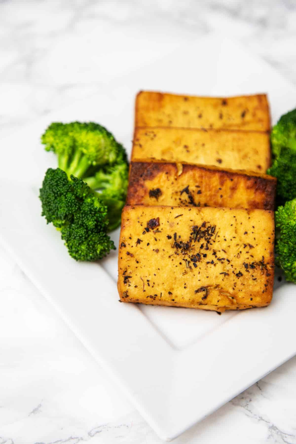 Close up photo of 4 slices of baked tofu on plate with broccoli