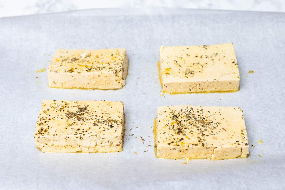 Four slabs of seasoned uncooked tofu on parchment paper