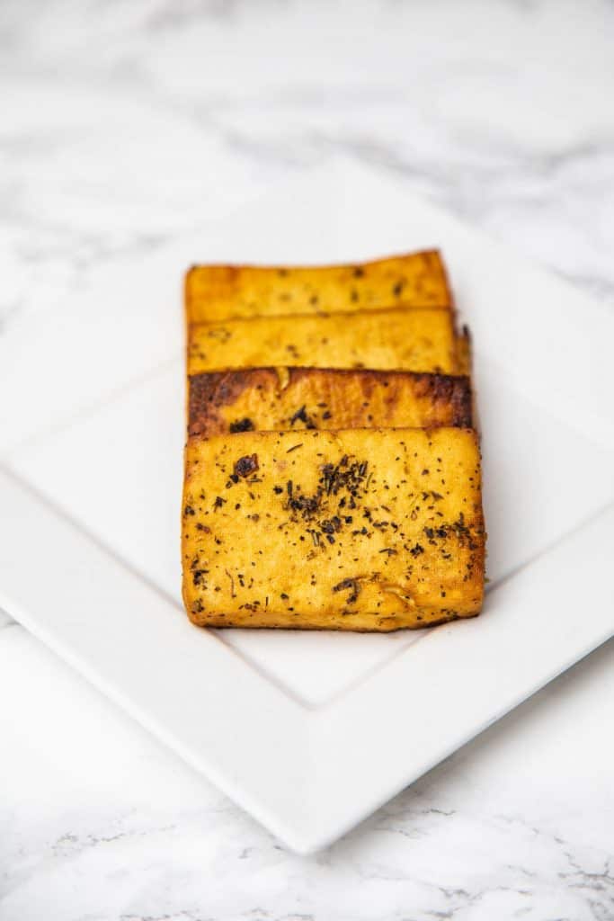 Four slices of baked tofu on plate on white marble counter