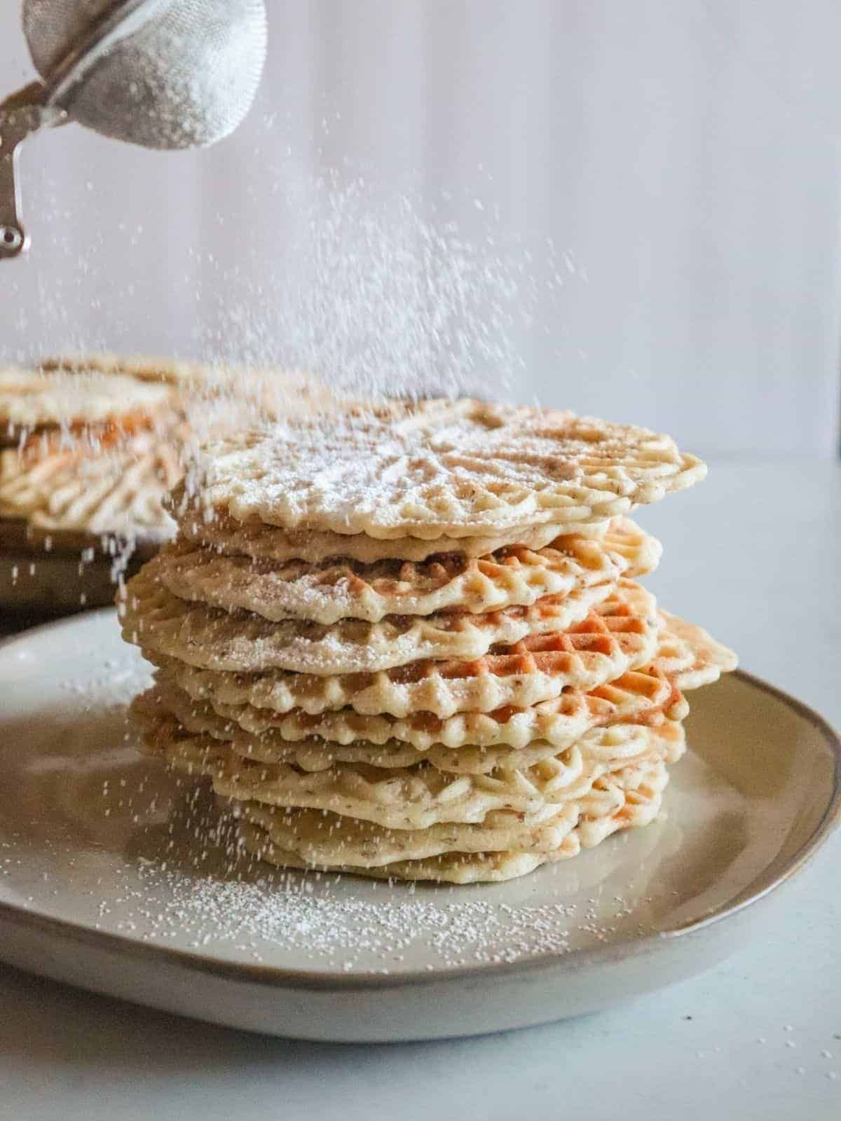 Stack of pizzelles on plate with powered sugar sprinkling on top