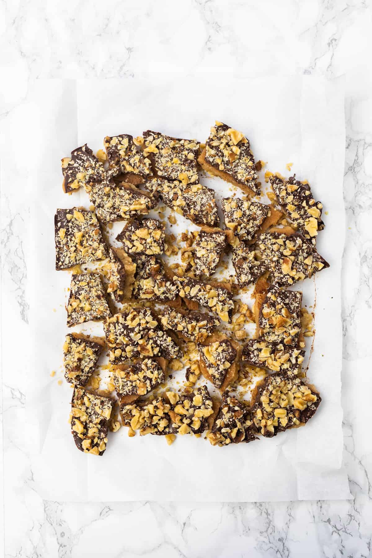 Broken up pieces of English toffee on piece of parchment paper on marble countertop