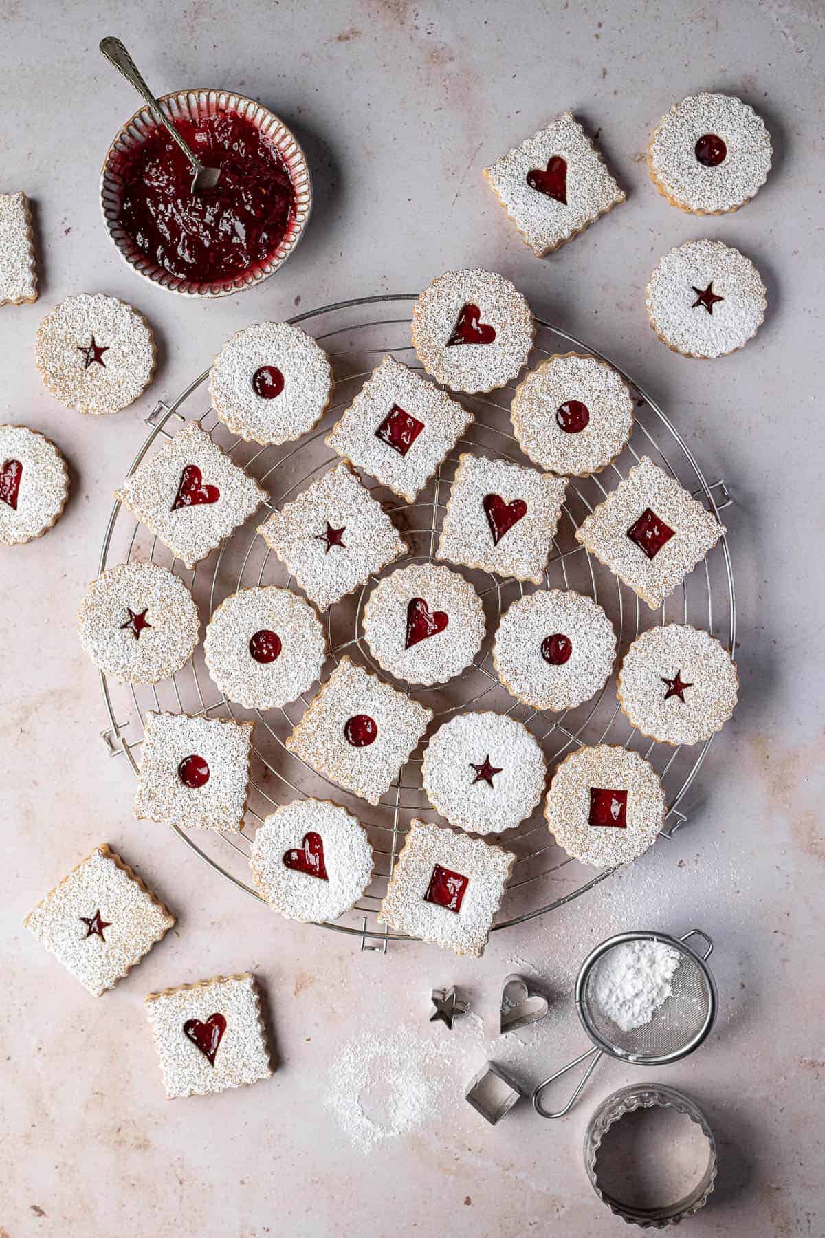 Linzer cookies on round wire cooling rack with jam and cookie cutters off to side