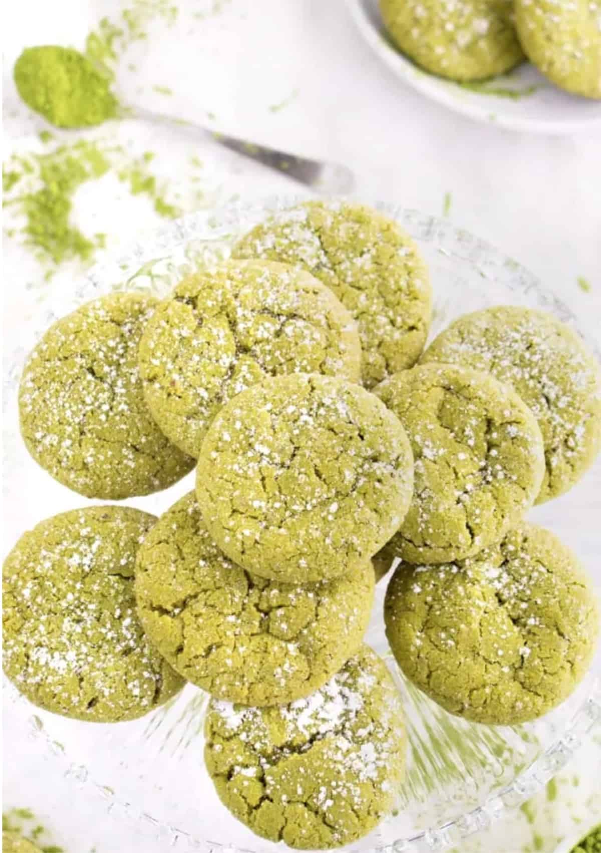 Green matcha cookies on a clear dish with spoonful of matcha off to side