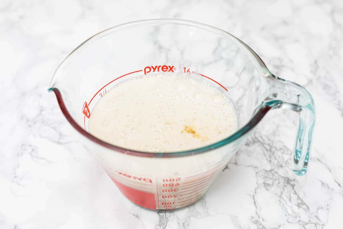 2 cups of non-dairy milk with apple cider vinegar in glass Pyrex measuring cup on white marble surface