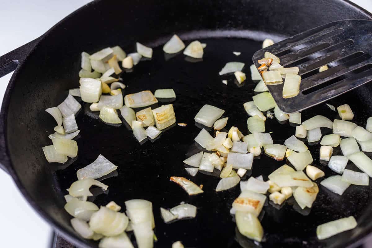 Chopped onion and garlic in cast iron pan on stove with spatula