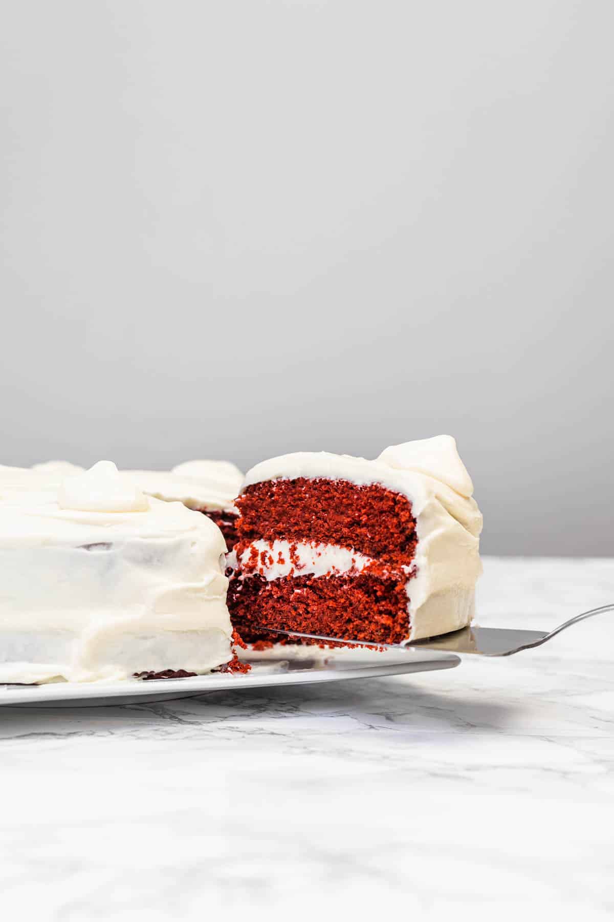 Slice of red velvet cake being lifted out of cake on plate with a cake server