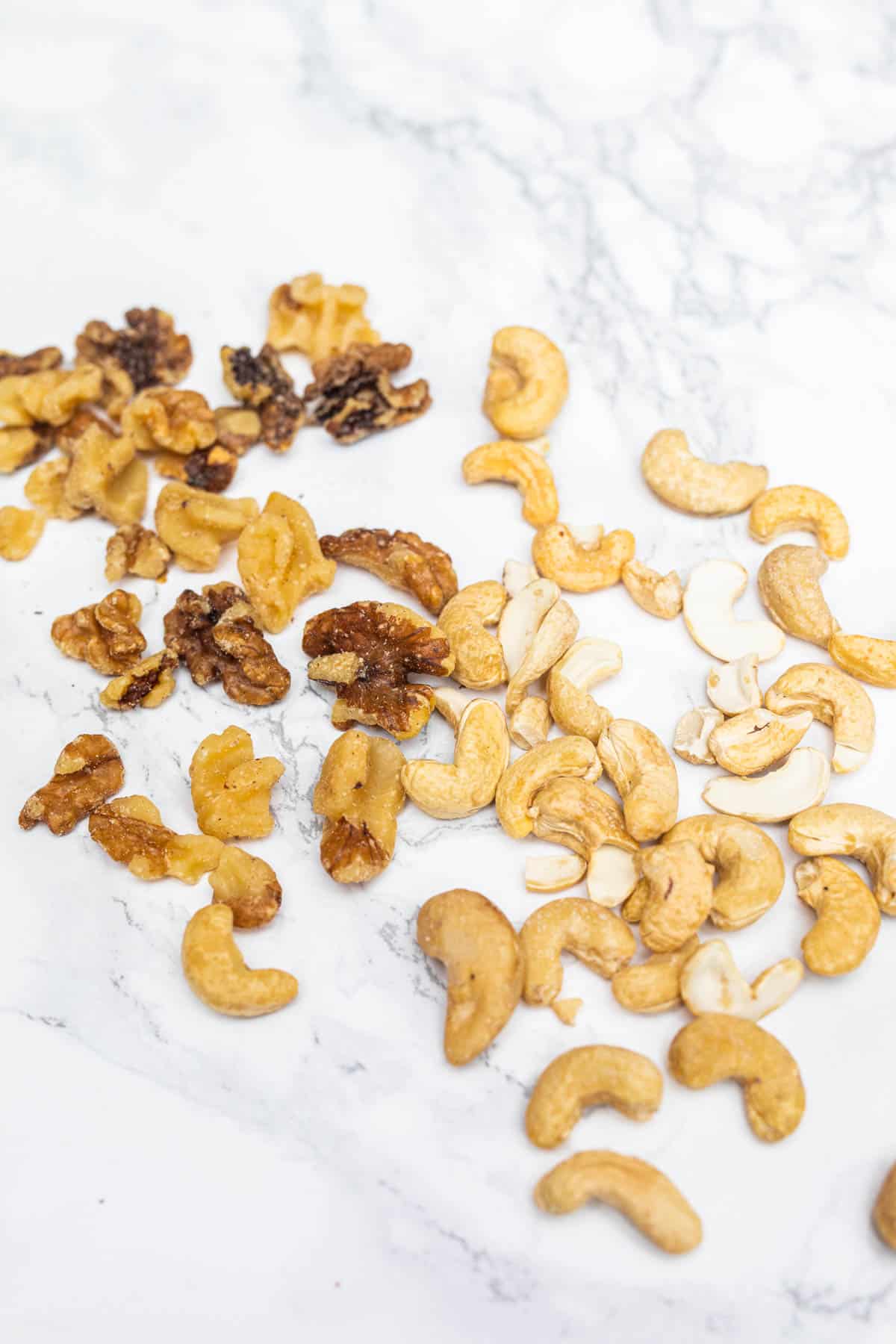 Raw walnuts and cashews scattered on white marble surface