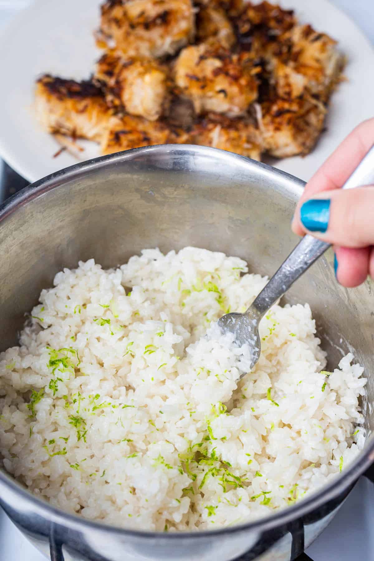 Hand fluffing cooked coconut rice with lime zest with a fork in a saucepan on the stove