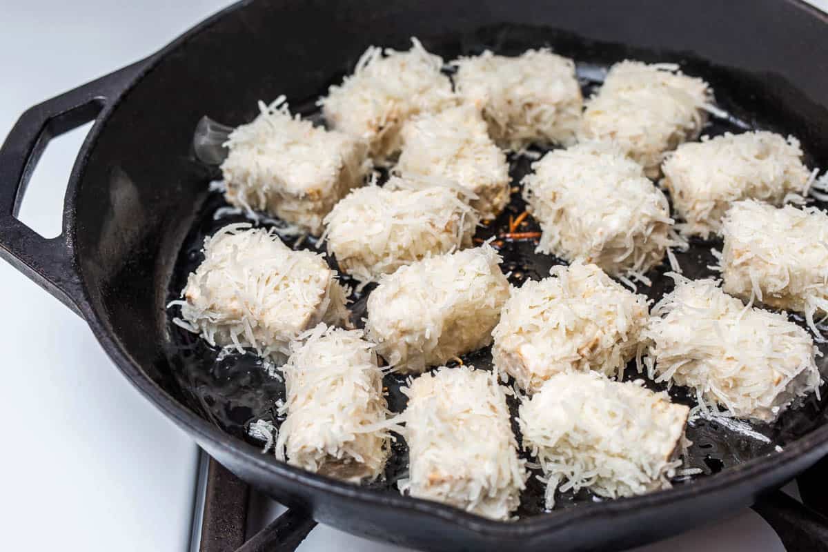 Tofu cubes coated in shredded coconut in cast iron pan