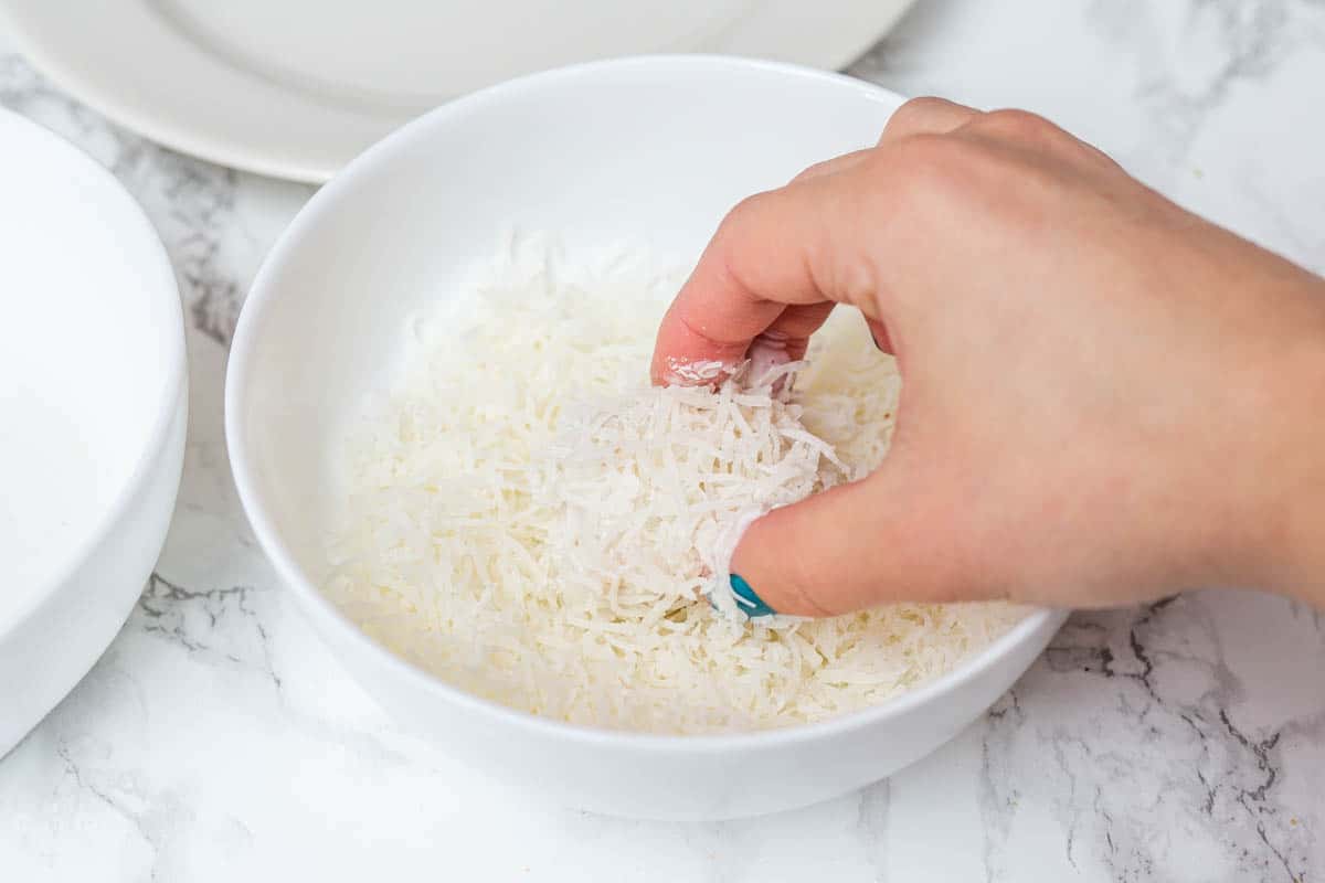 Hand rolling tofu cube in bowl of shredded coconut