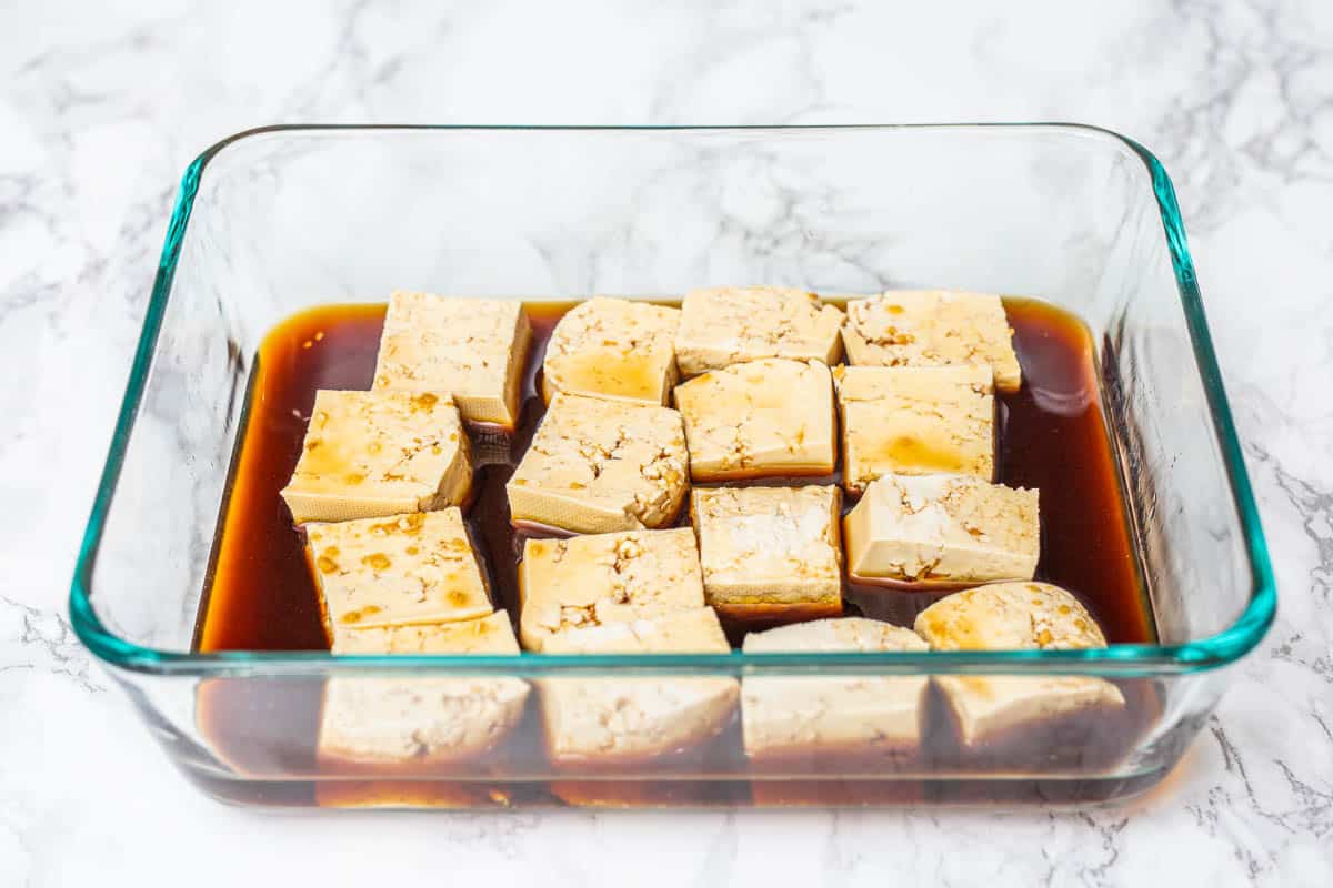 Cubed tofu in dish of marinade on white marble surface