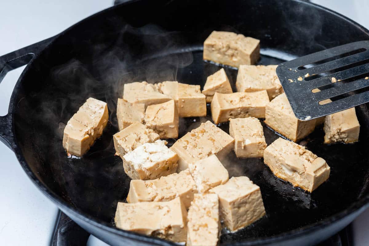 Cubed tofu cooking in cast iron pan on stove
