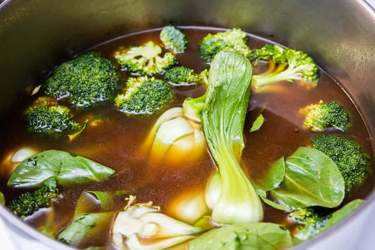 Stock pot with vegan pho broth with broccoli and baby bok choy
