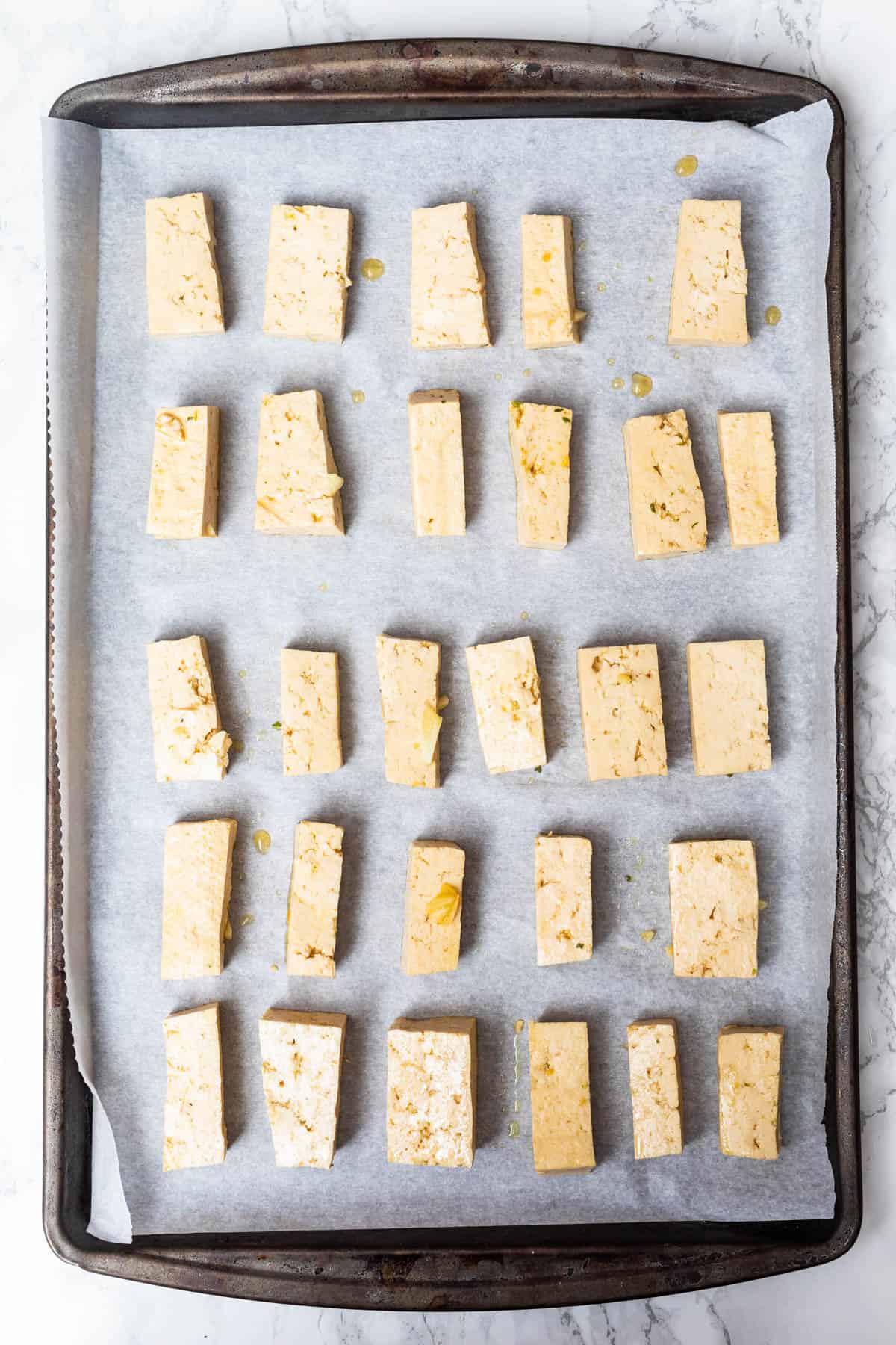 Raw pieces of tofu on parchment paper on baking sheet