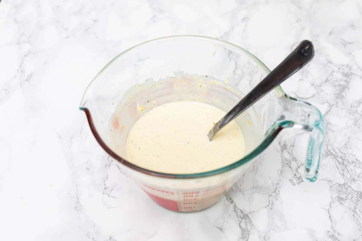 Vegan caesar dressing in glass measuring cup with spoon on white marble counter
